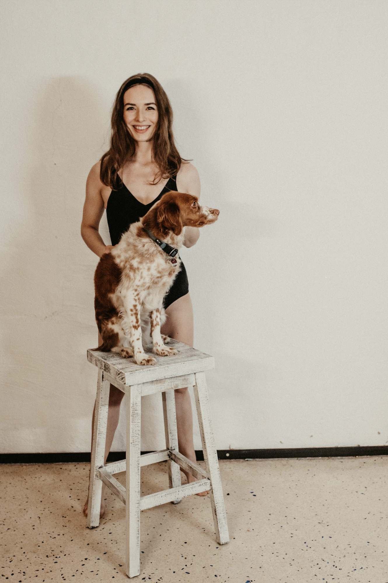 Paula Hauss: Frau posiert vor Wand mit Hund, der auf einem Hocker sitzt